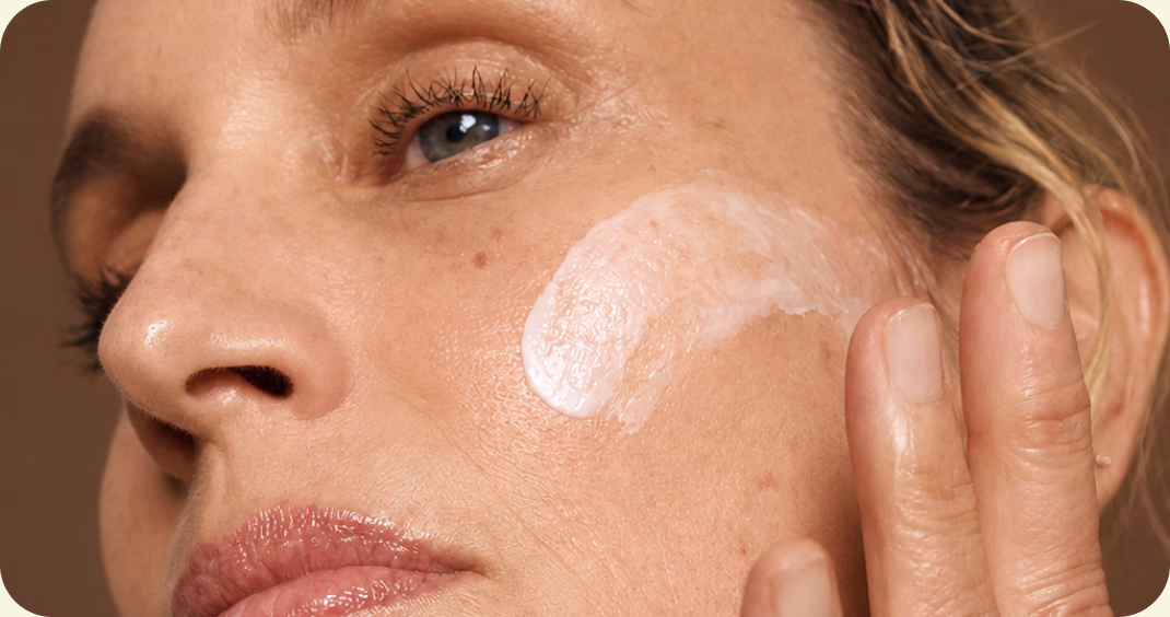 Close-up of a woman smoothing a stroke of white cream onto her cheekbone